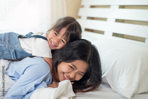 Happy Asian family loving children, kid and her sister kissing and relaxing together in bed