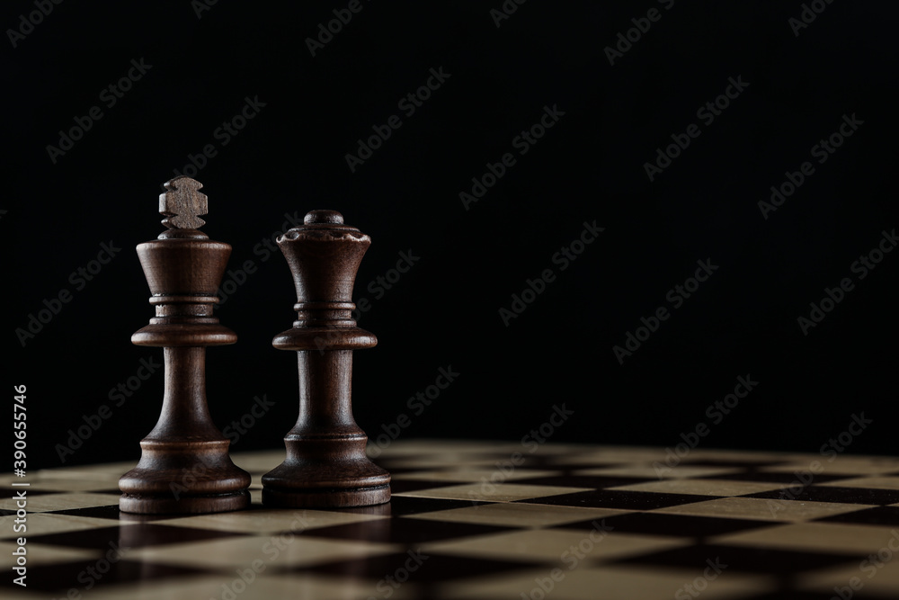 king and queen chess pieces on chessboard on black background king and queen chess pieces on chessboard on black background