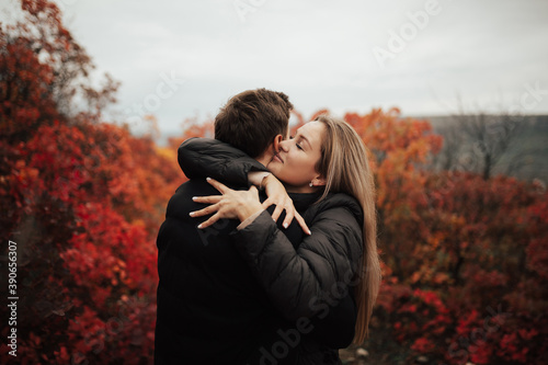 Man and woman with closed eyes hugging on the background of red autumn trees. 