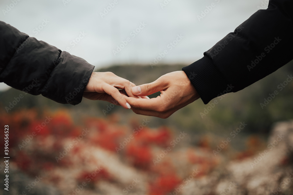 Close up of arms of young couple in love holding hands. The holding hands together in autumn park. Romantic relationship.