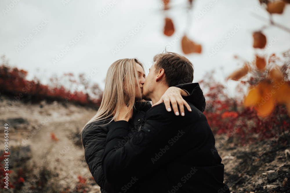 Close-up of a young beautiful couple kissing on a autumn day against the background of a red leaves.