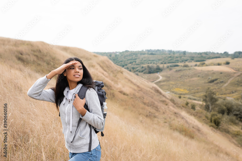 Smiling african american woman holding backpack and looking away during trip on hill Smiling african american woman holding backpack and looking away during trip on hill