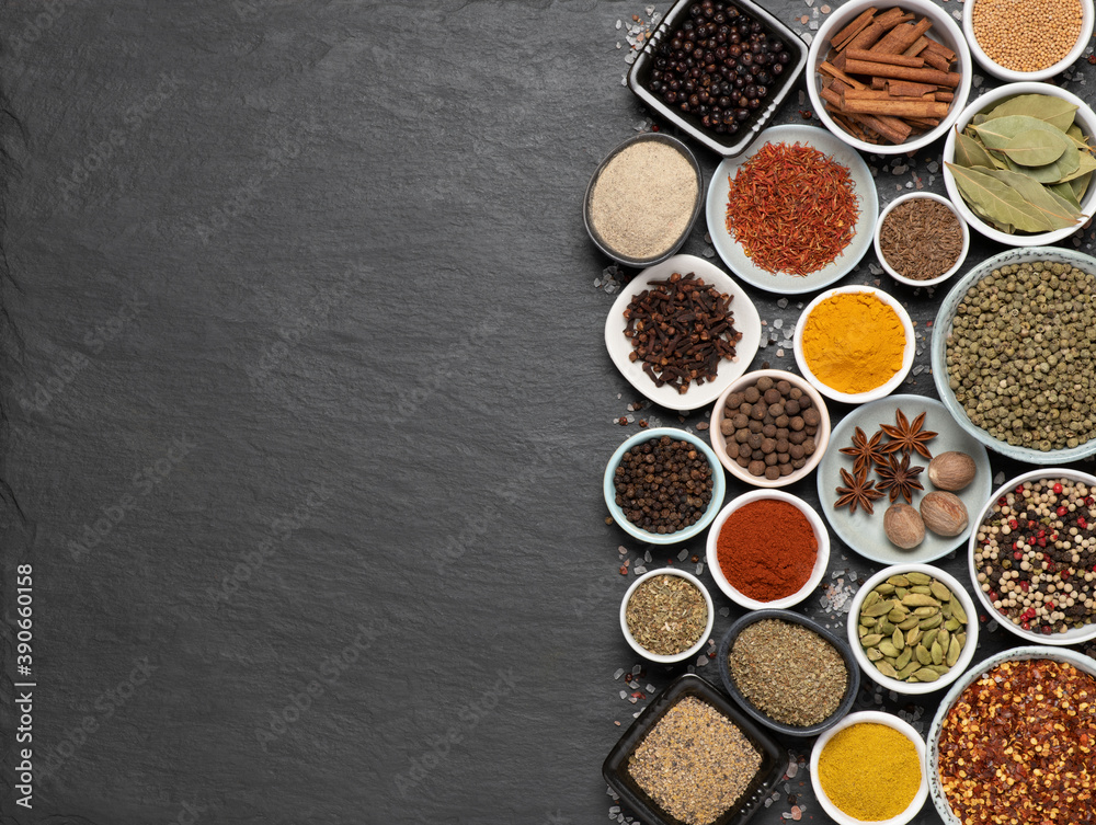 Assortment of aromatic spices and herbs in small bowls on black stone background with copy space