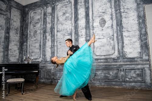 a young man in a black suit is dancing with a girl in a turquoise dress in the dance hall © константин константи