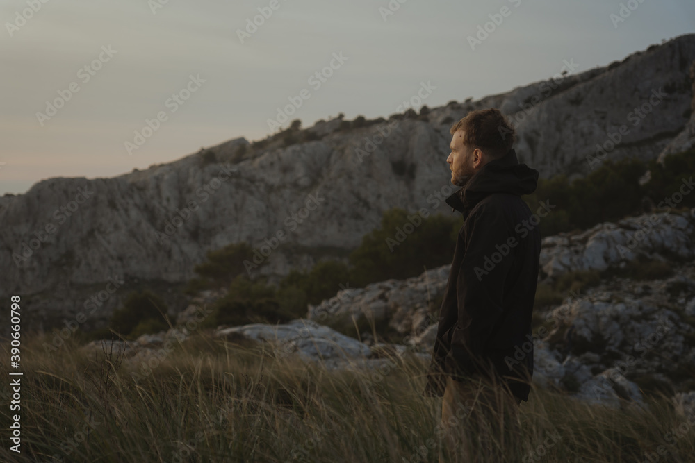 Blond man in profile looking at sunrise waiting for the golden hour from a mountain with weeds in the surroundings