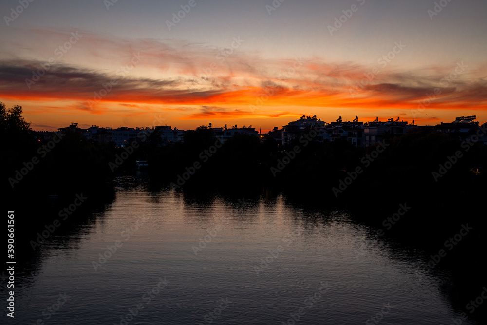 Fototapeta premium Sunset with Trees and City Silhouettes Against A Beautifully Colored Sky At River Manavgat 