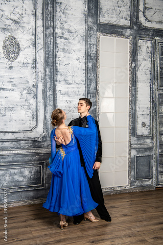 young man dancing with a girl in a blue ballroom dress in a gray dance hall © константин константи