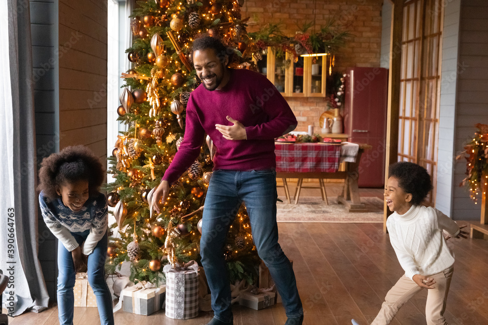 Overjoyed African American father with adorable kids having fun on winter holidays, happy family with daughter and son laughing and dancing to music near decorated Christmas tree at home