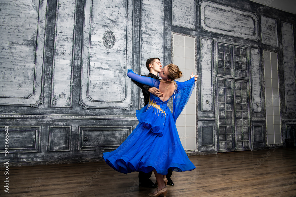 young man dancing with a girl in a blue ballroom dress in a gray dance hall