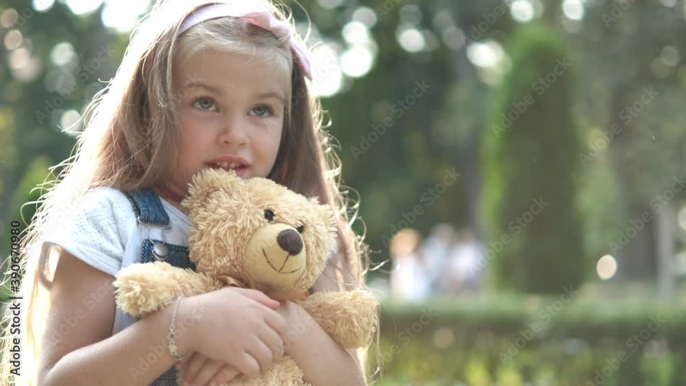 Happy little preeschool girl playing with her favorite teddy bear toy outdoors in summer park. Happy little preeschool girl playing with her favorite teddy bear toy outdoors in summer park.