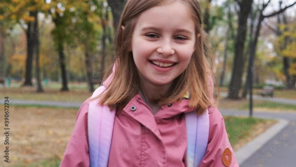 Smiling little girl with backpack walking after school in autumn park