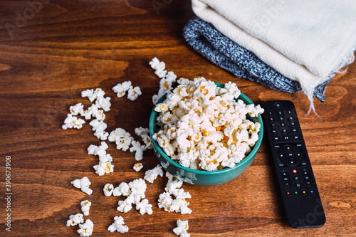 Popcorn, remote control and blanket on wooden table Sofa, blanket and film, conceptual of rest and relaxation at home