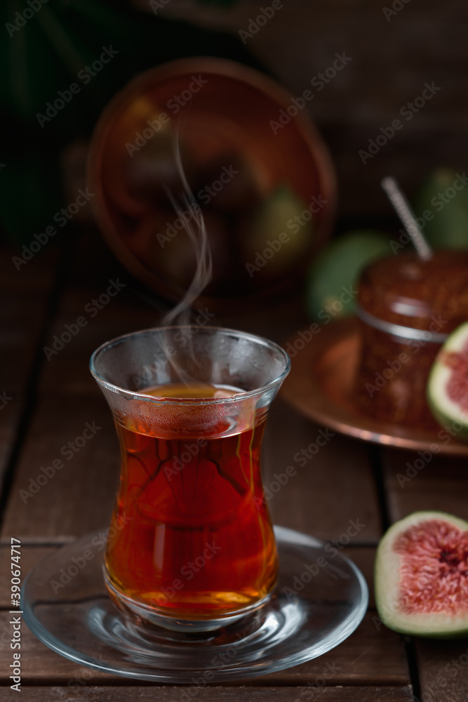 Tea in a traditional armudu glass, half a ripe fig next to it. Dessert in the background - fig jam. vintage wooden table, close-up Tea in a traditional armudu glass, half a ripe fig next to it. Dessert in the background - fig jam. vintage wooden table, close-up