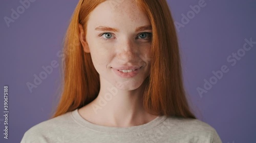 A close-up view of an attractive young woman is opening her eyes and looking to the camera standing isolated over a violet background photo