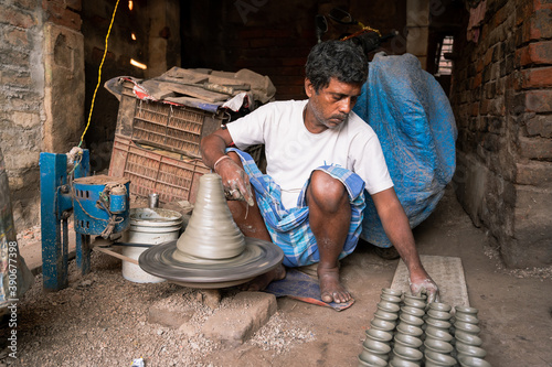 Indian potter making small pot or Diya for Diwali with clay on potters wheel in his small factory. Manufacturing traditional handicraft with clay. photo