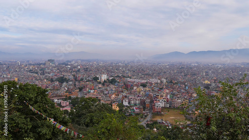Panorama view of densely populated city center of Kathmandu, capital of Nepal, with visible smog viewed from Buddhist temple complex Swayambhunath with colorful prayer flags, trees and mountains.