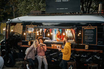 multiethnic group of  people socializing while eating outdoor in front of modified truck for fast food