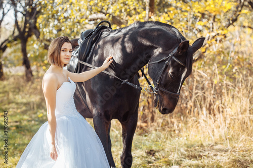 woman in white wedding dress walking with a horse in autumn park. horseback riding © Dmytro Titov