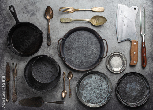 Old vintage tableware and kitchen utensils on rustic stone background, top view. Various metallic plates, bowls, cast-iron pan, cutlery. Set of assorted antique dish ware, kitchen and cooking concept photo