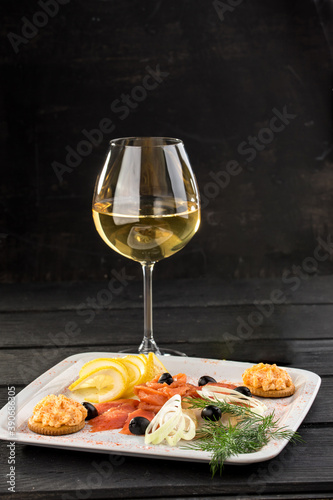 glass of white wine with fish platter snack on black background