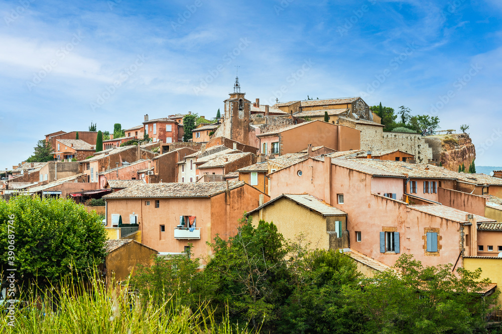 Old Provencal village on a cliff with houses from ocre clay behind bushes - Rousillon, Provence, France