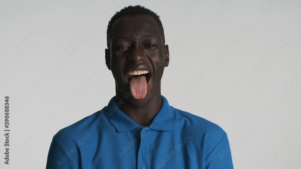Fototapeta premium Attractive funny African guy showing tongue on camera and laughing over white background. Joyful expression
