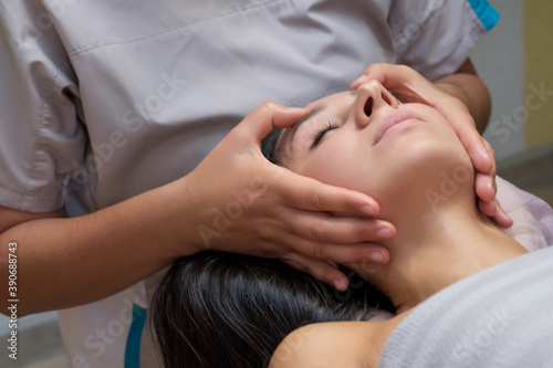 Calm beautiful woman in massage salon receiving face massage.