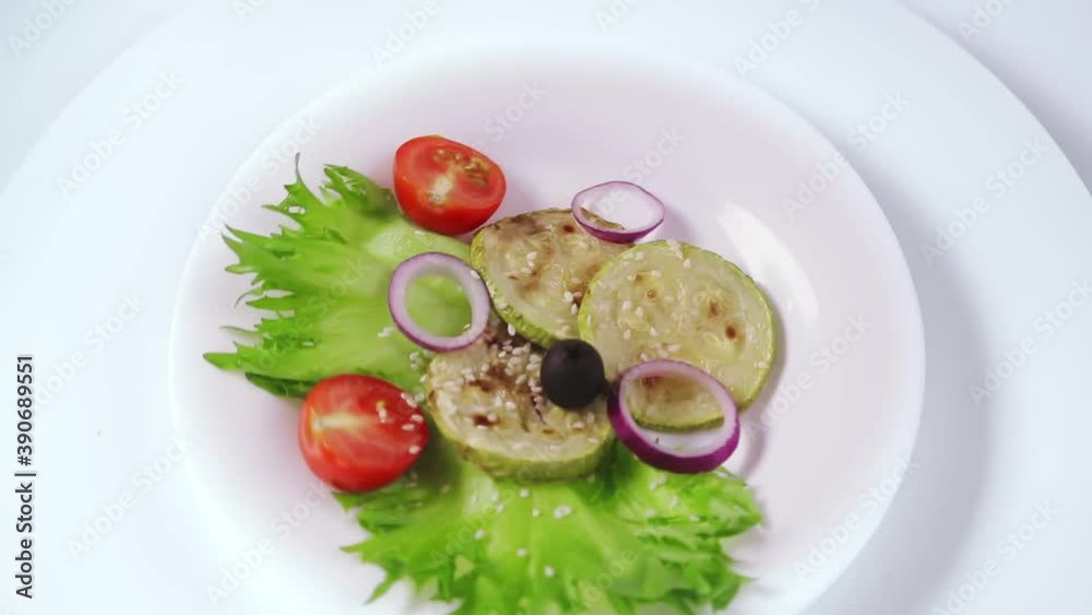 Grilled zucchini in Greek in a white plate on a white plate rotates in a circle Grilled zucchini in Greek in a white plate on a white plate rotates in a circle