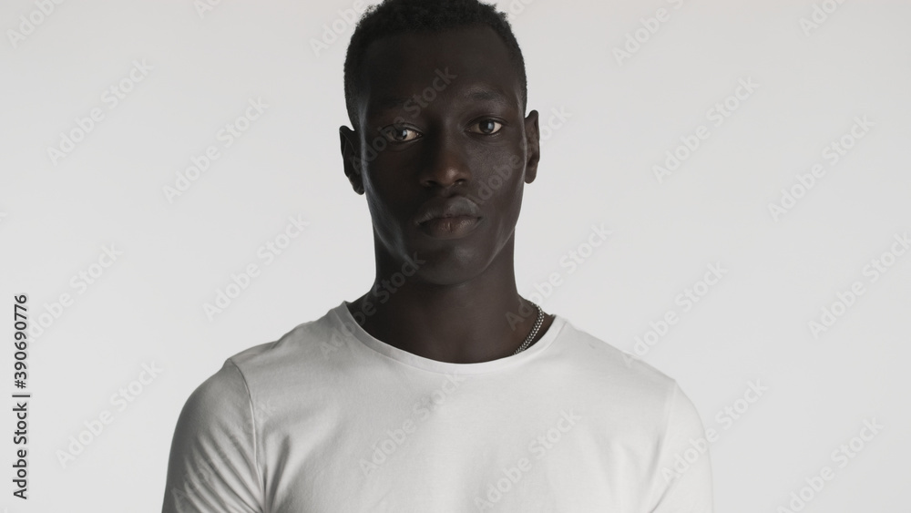Obraz premium African American guy wearing white t-shirt posing on camera with serious look over white background