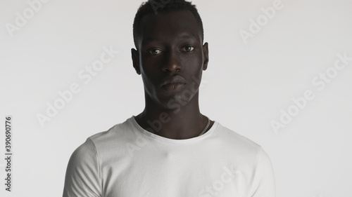 African American guy wearing white t-shirt posing on camera with serious look over white background