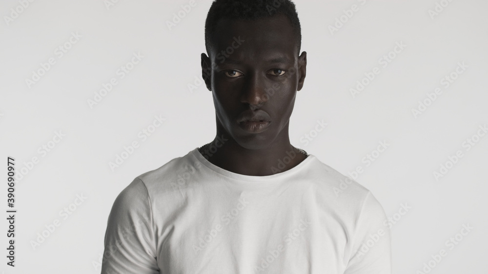 Angry African American guy wearing t-shirt looking aggressive on camera with over white background Angry African American guy wearing t-shirt looking aggressive on camera with over white background