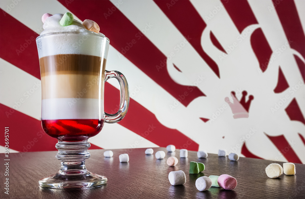 Caffe latte layered with milk in a high drinking glass with marshmallows on top of milk foam. There are marshmallow spread out on the wooden table next to the glass. Alice in Wonderland style