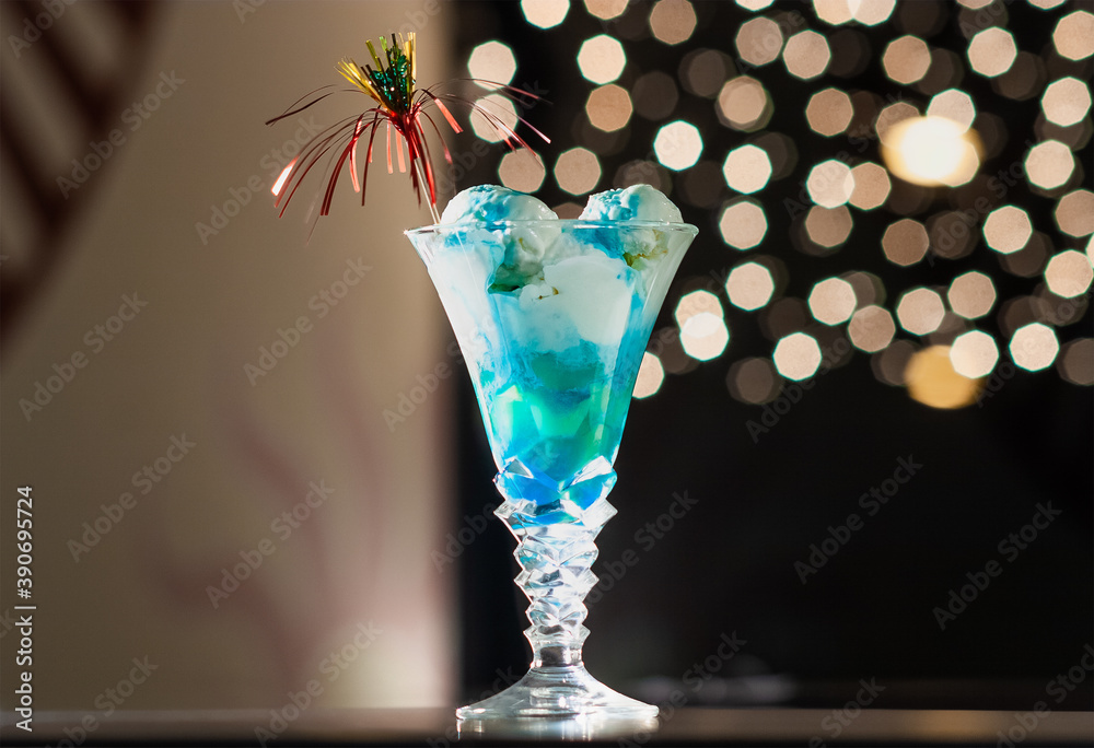 Blue Caterpillar Cocktail. Ice cream balls in a crystal glass are filled with blue liqueur and a transparent straw is decorated in a Happy New Year's style