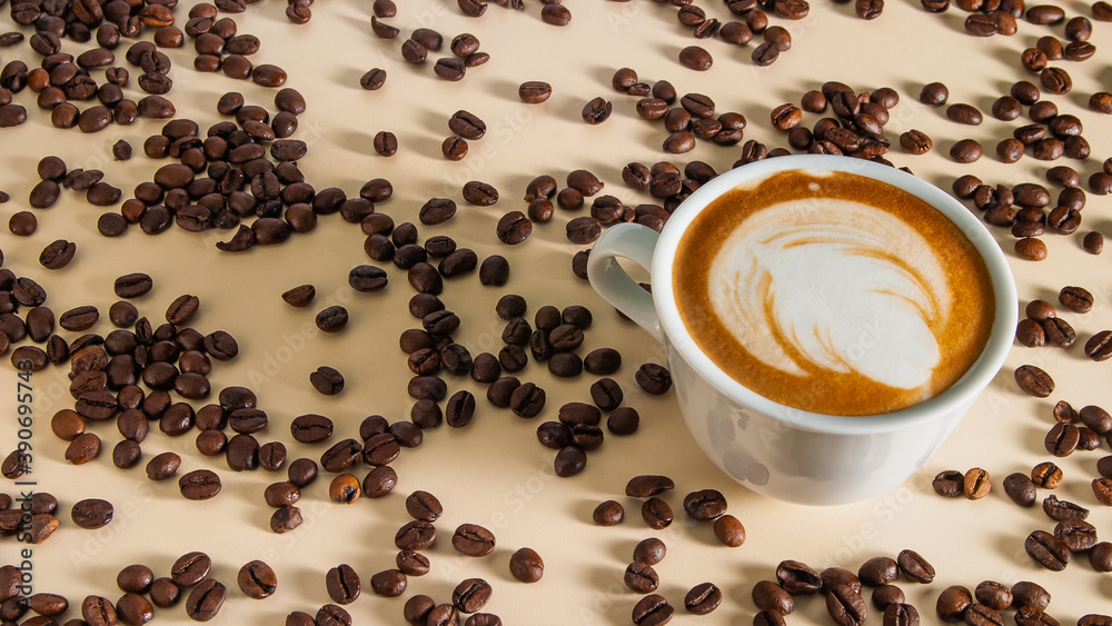 Cappuccino with a beautiful pattern on the milk foam in a white cup on the table cream color and scattered around the roasted coffee beans