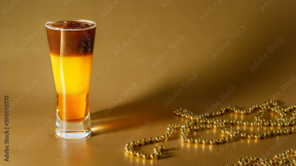 Cold coffee cocktail with layers of liqueur and orange juice with ice on a gold background with pearl beads