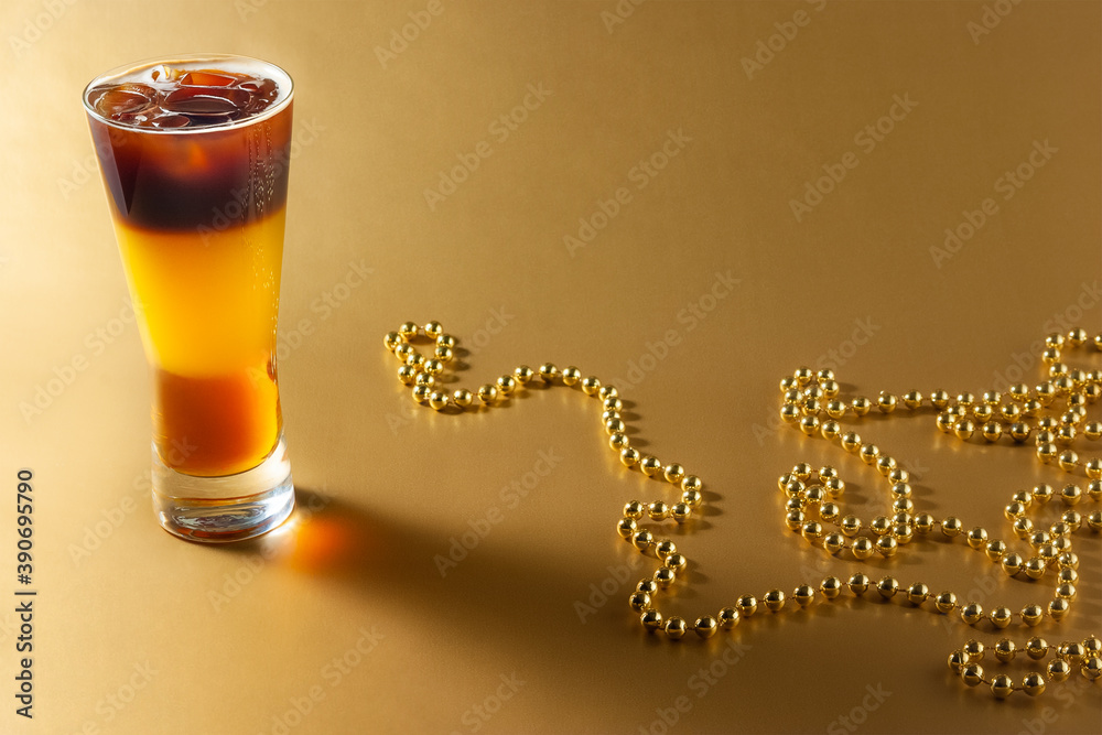 Cold coffee cocktail with layers of liqueur and orange juice with ice on a gold background with pearl beads