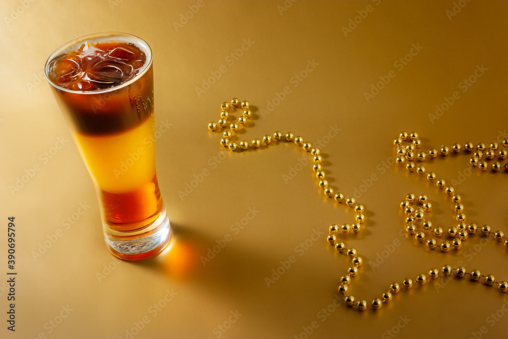 Cold coffee cocktail with layers of liqueur and orange juice with ice on a gold background with pearl beads