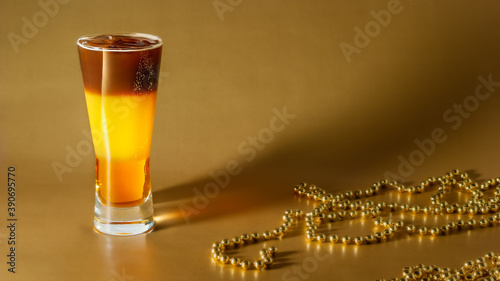 Obraz na płótnie Cold coffee cocktail with layers of liqueur and orange juice with ice on a gold background with pearl beads w salonie