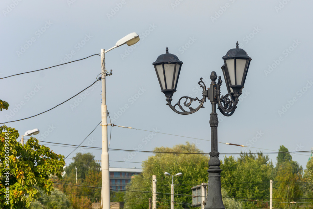 Retro street lamp with forged iron elements next to modern urban lighting pole. Concept of past and present, comparison, technology development