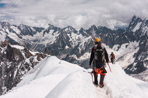 A couple of mountaineers walk through the snow in the Alps with a stunning mountain range as a background