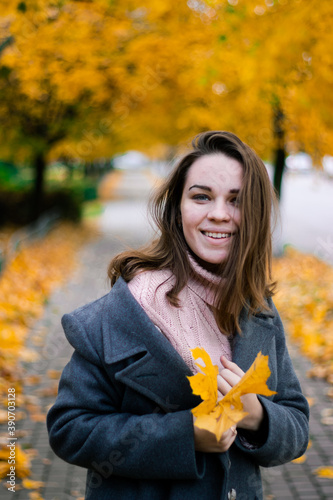 beautiful girl in an autumn coat with yellowed maple leaves in her hands