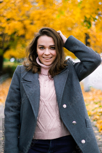 beautiful girl in an autumn coat walks in the park with autumn trees with yellowed leaves