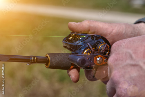 hand with spinning and reel on the evening summer lake. Fishing on the lake at sunset. Fishing background.