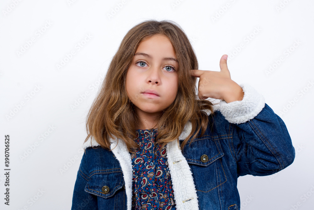 Unhappy Little caucasian girl with beautiful blue eyes wearing denim jacket standing over isolated white makes suicide gesture and imitates gun with hand, curves lips keeps two fingers on temple, Unhappy Little caucasian girl with beautiful blue eyes wearing denim jacket standing over isolated white makes suicide gesture and imitates gun with hand, curves lips keeps two fingers on temple,