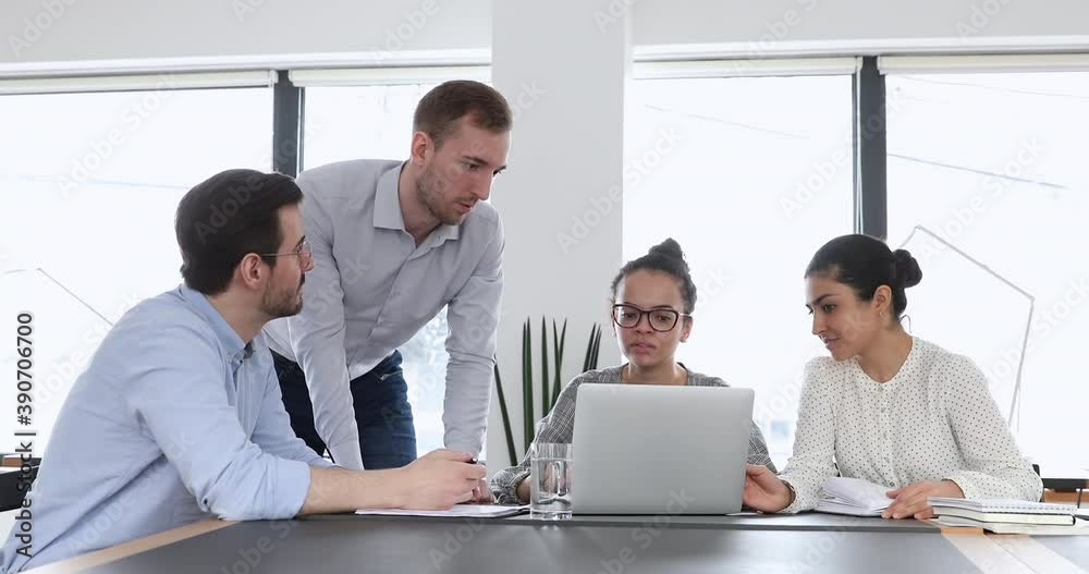 Serious team leader explaining computer software or online project details to focused multiracial coworkers in office. Concentrated young mixed race colleagues working on business presentation. Serious team leader explaining computer software or online project details to focused multiracial coworkers in office. Concentrated young mixed race colleagues working on business presentation.