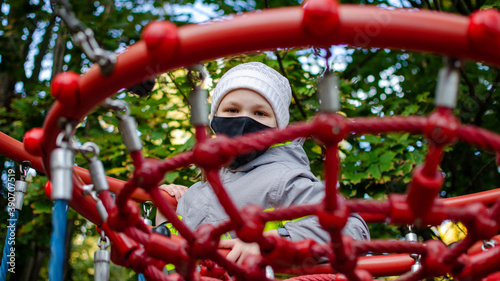 Fototapeta Naklejka Na Ścianę i Meble -  little girl wearing a mask plays on the playground