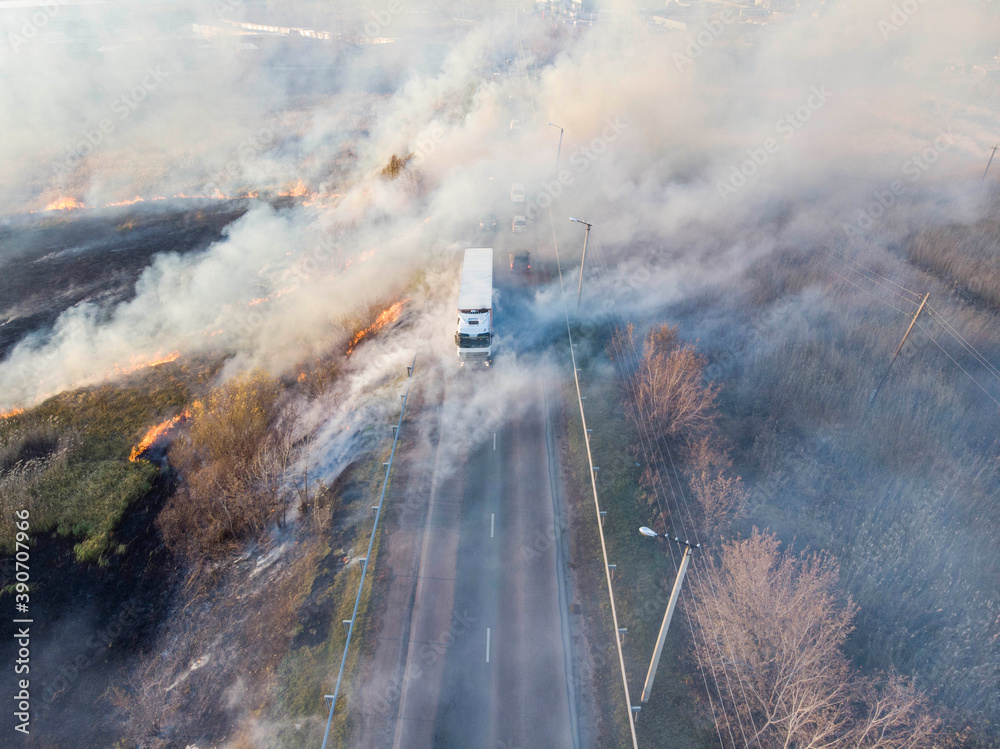 burning field of dead wood next to the road and moving vehicles, drone photography