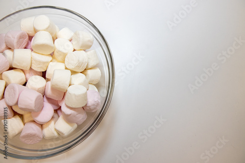 A bowl of delicious white and pink marshmallows on a white wooden table