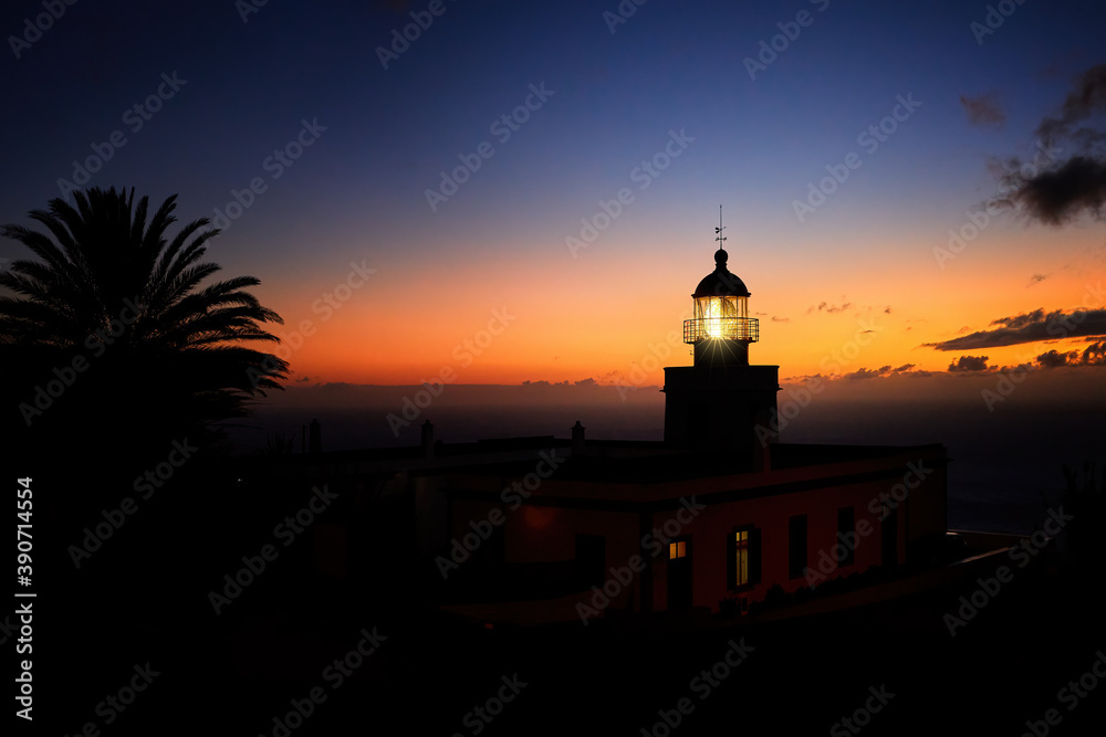 Silhouette of a glowing lighthouse against an orange evening sky.  Ponta do Pargo lighthouse, Madeira island, Portugal.