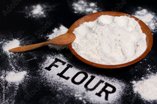 Cup with white flour. Wooden spoon. A several handfuls of flour. At the bottom of the inscription-flour.  photo